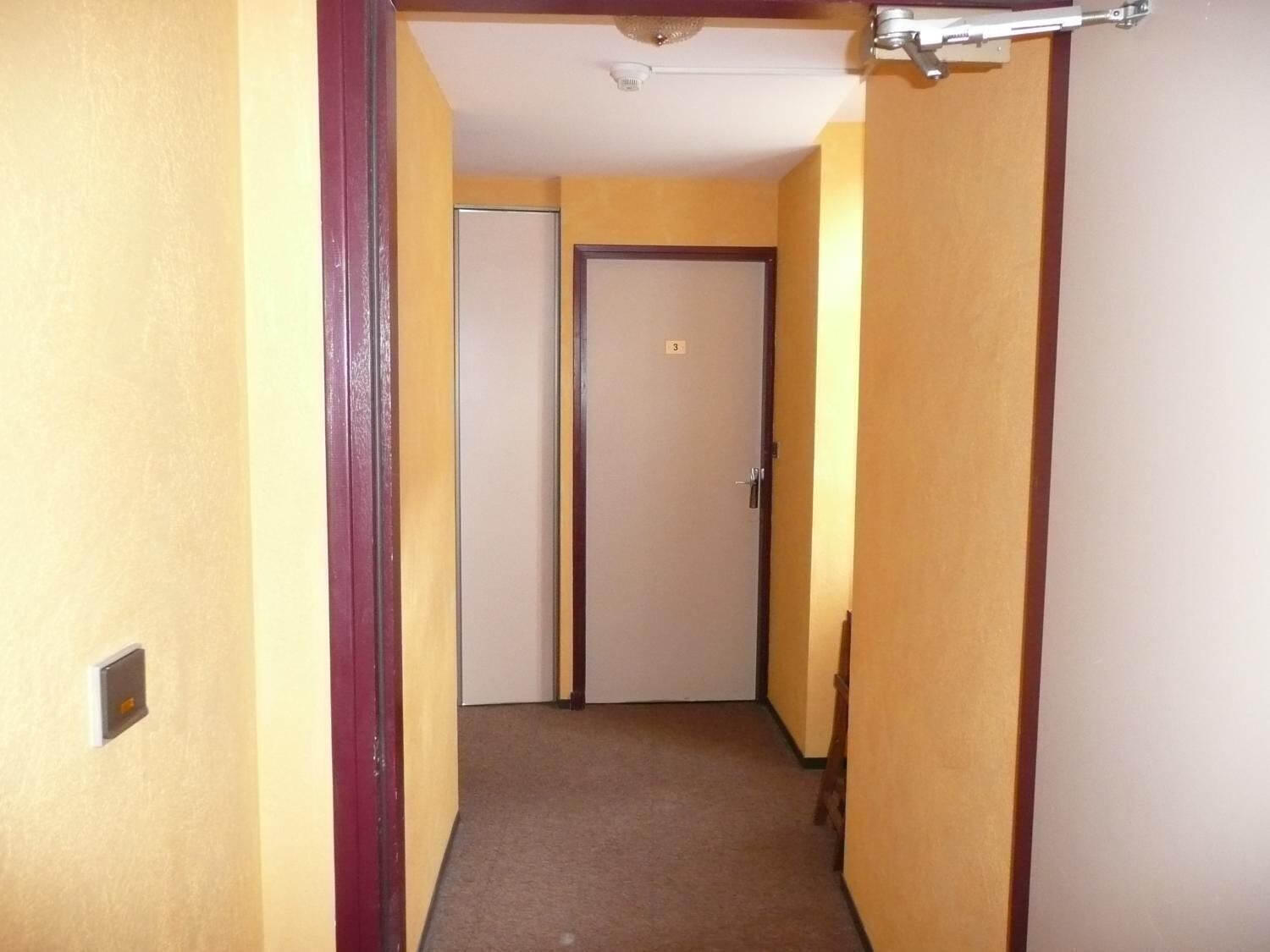 A narrow hallway with yellow walls and a carpeted floor.