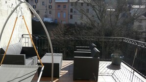 Un balcón al aire libre con muebles de mimbre, baranda de metal y una planta en maceta.