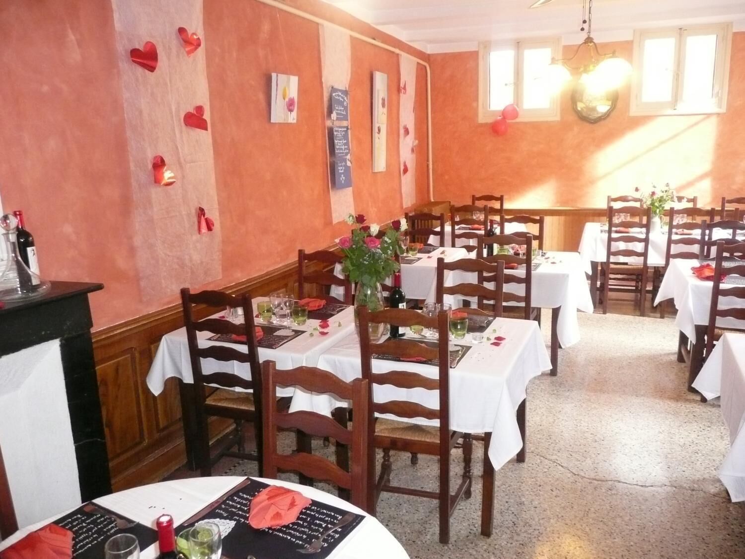 Un restaurant avec des chaises et des tables en bois, un lustre et des décorations en forme de cœur sur les murs.