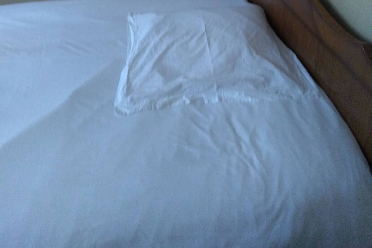 Un lit bien fait, avec un oreiller et une table de chevet sur laquelle se trouve une lampe.