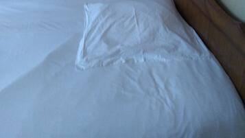 A neatly made bed with a pillow and a bedside table with a lamp.