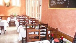 Un restaurante con sillas de madera y manteles blancos, un menú en una pizarra y un ventanal con luz natural.