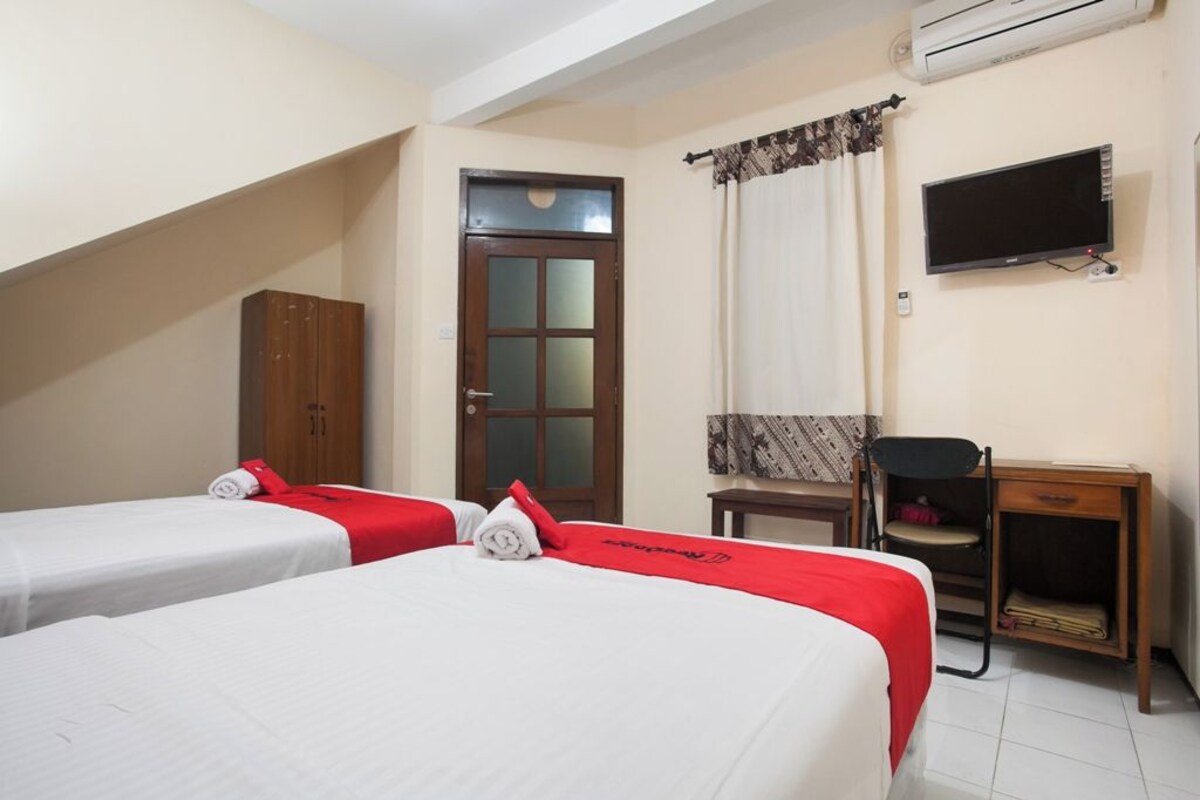 Une chambre d’hôtel avec deux lits, un bureau, une chaise, un téléviseur et un appareil de climatisation.