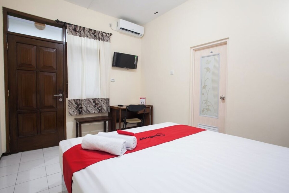 Une chambre d’hôtel avec un lit, un bureau, une chaise, une télévision et une porte.