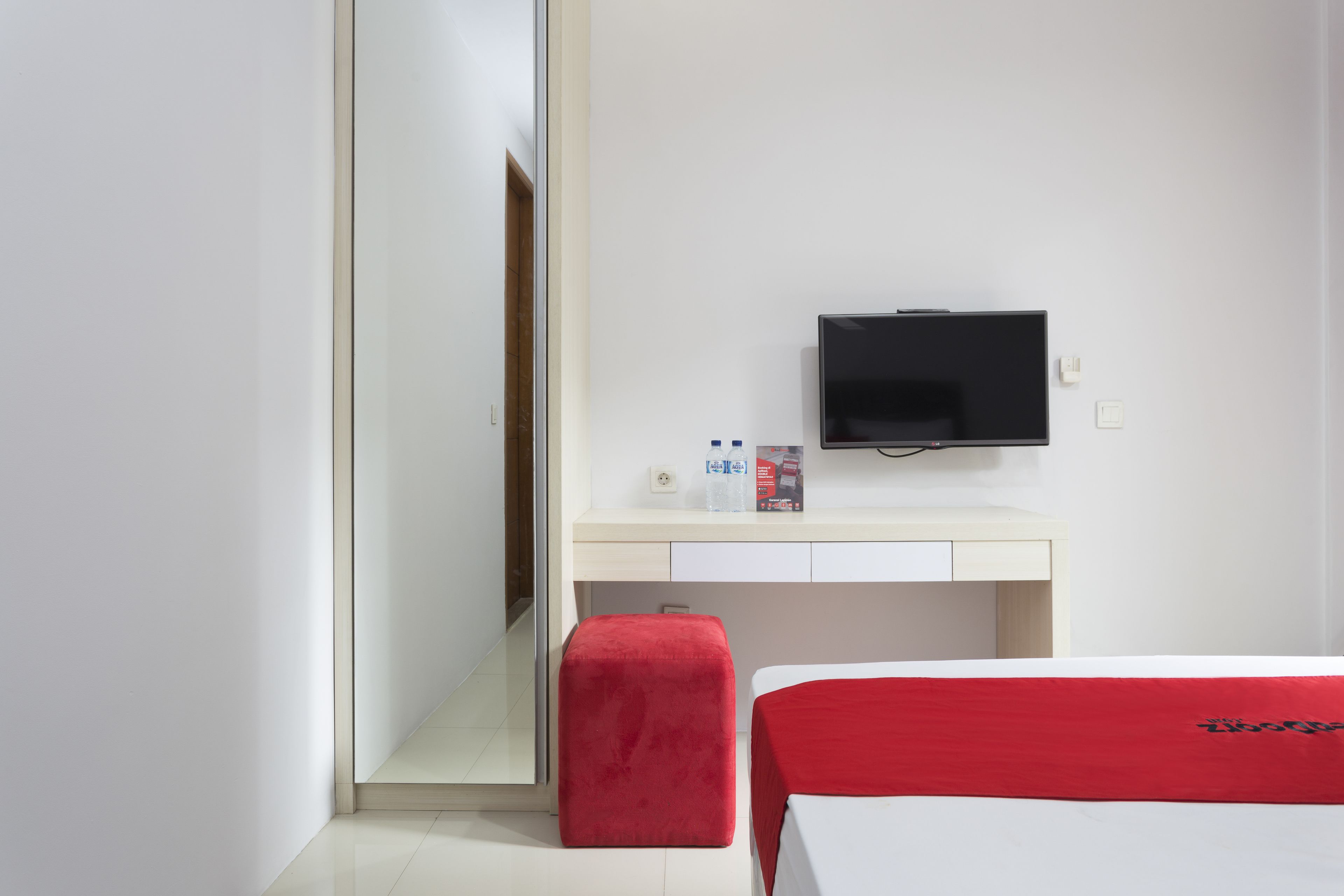 A hotel room with a bed, a desk, a television, and a red chair.
