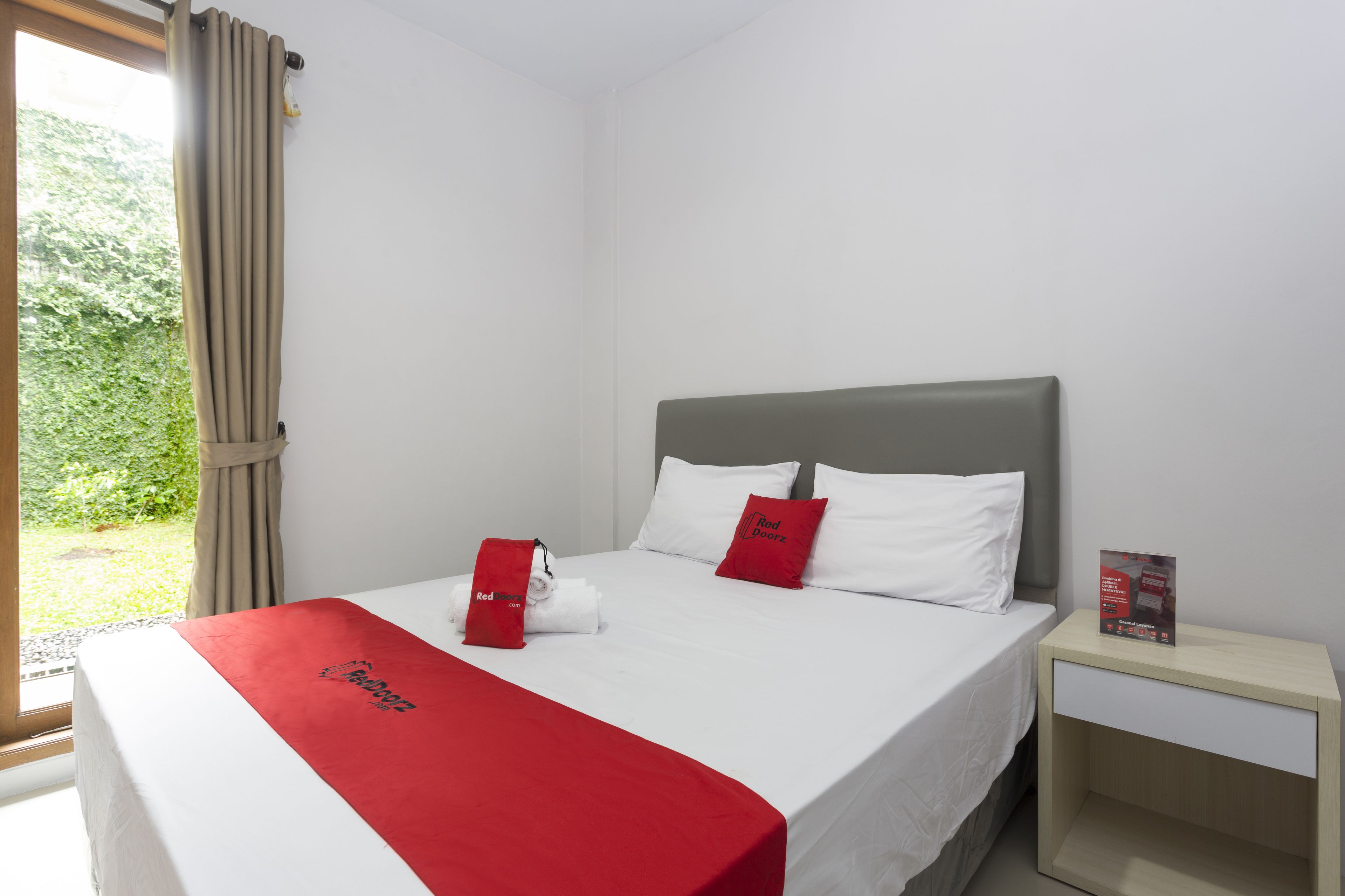 Ein Hotelzimmer mit Bett, Nachttisch und einem fensterbepflanzten Fenster.