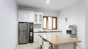 A modern kitchen with white cabinets, a stainless steel refrigerator, a wooden dining table, and a microwave. - RedDoorz Plus near Cilandak Town Square 2 (Jakarta)