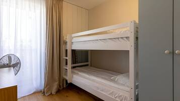 A bunk bed room with a desk, a fan, and a wardrobe.