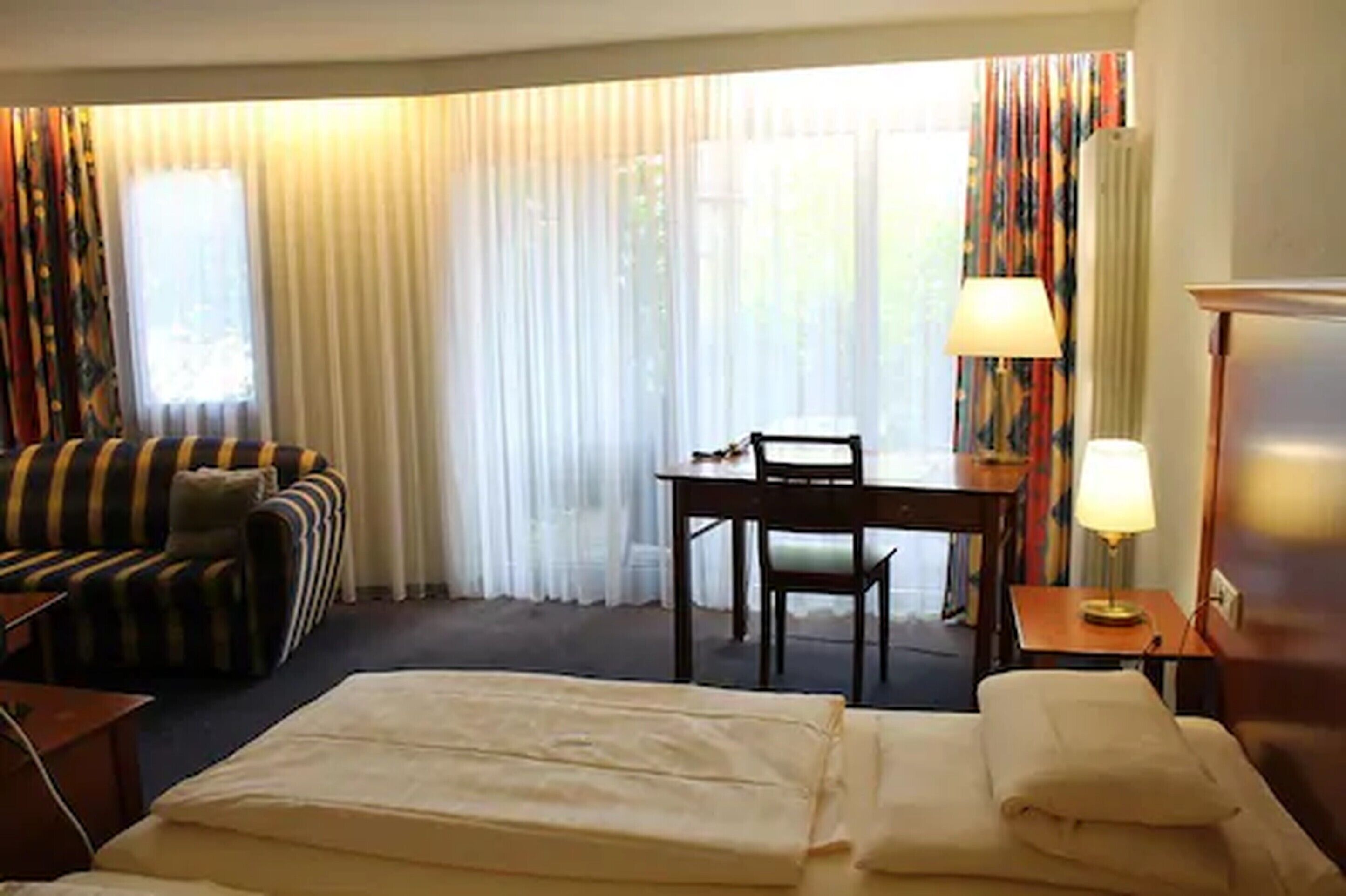 A hotel room with a bed, a sofa, a dining table with chairs, and a lamp.