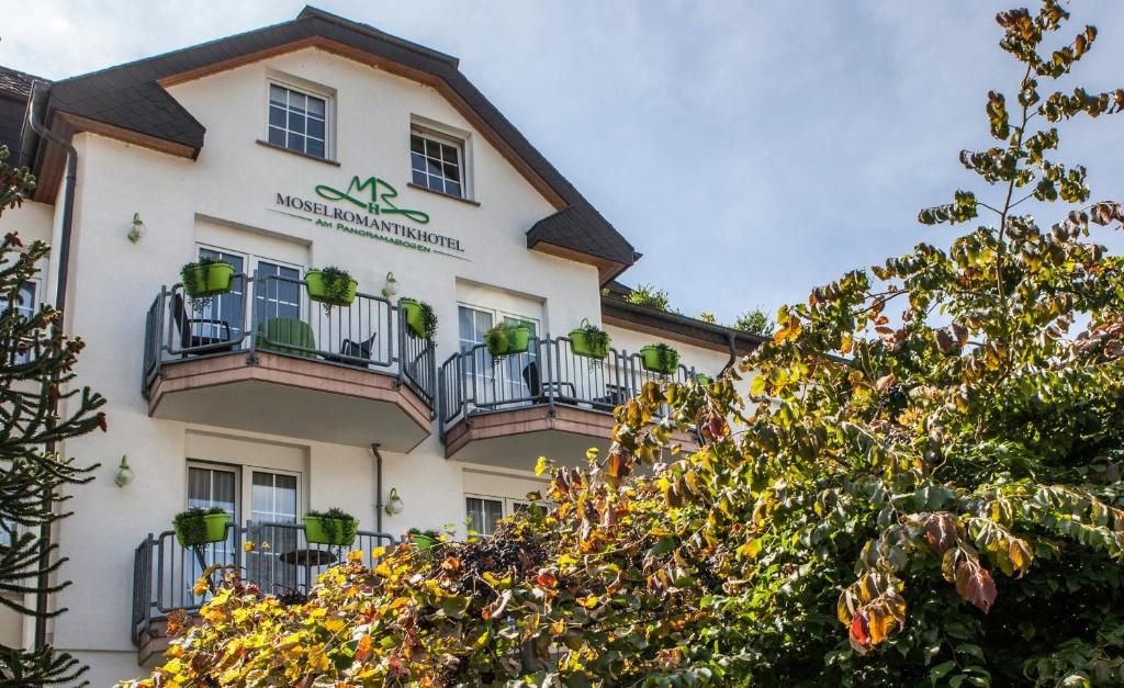 Ein Hotel mit weißer Fassade, Balkonen mit Grünpflanzen und einem Schild mit der Aufschrift 'MOSELROMANTIKHOTEL'.