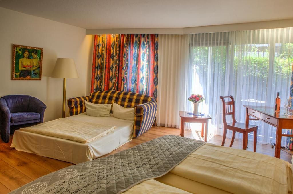 A hotel room with a bed, a chair, a desk, and a window with curtains.