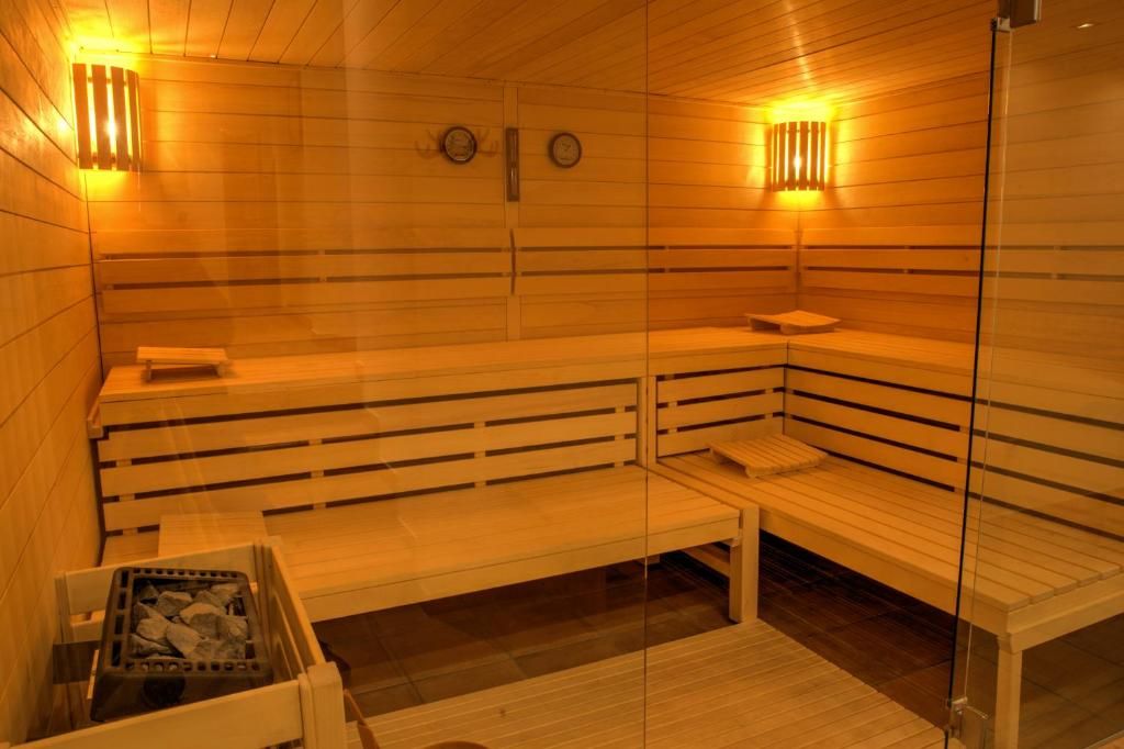 A sauna with benches and a glass partition, wooden walls, and wall-mounted clocks.