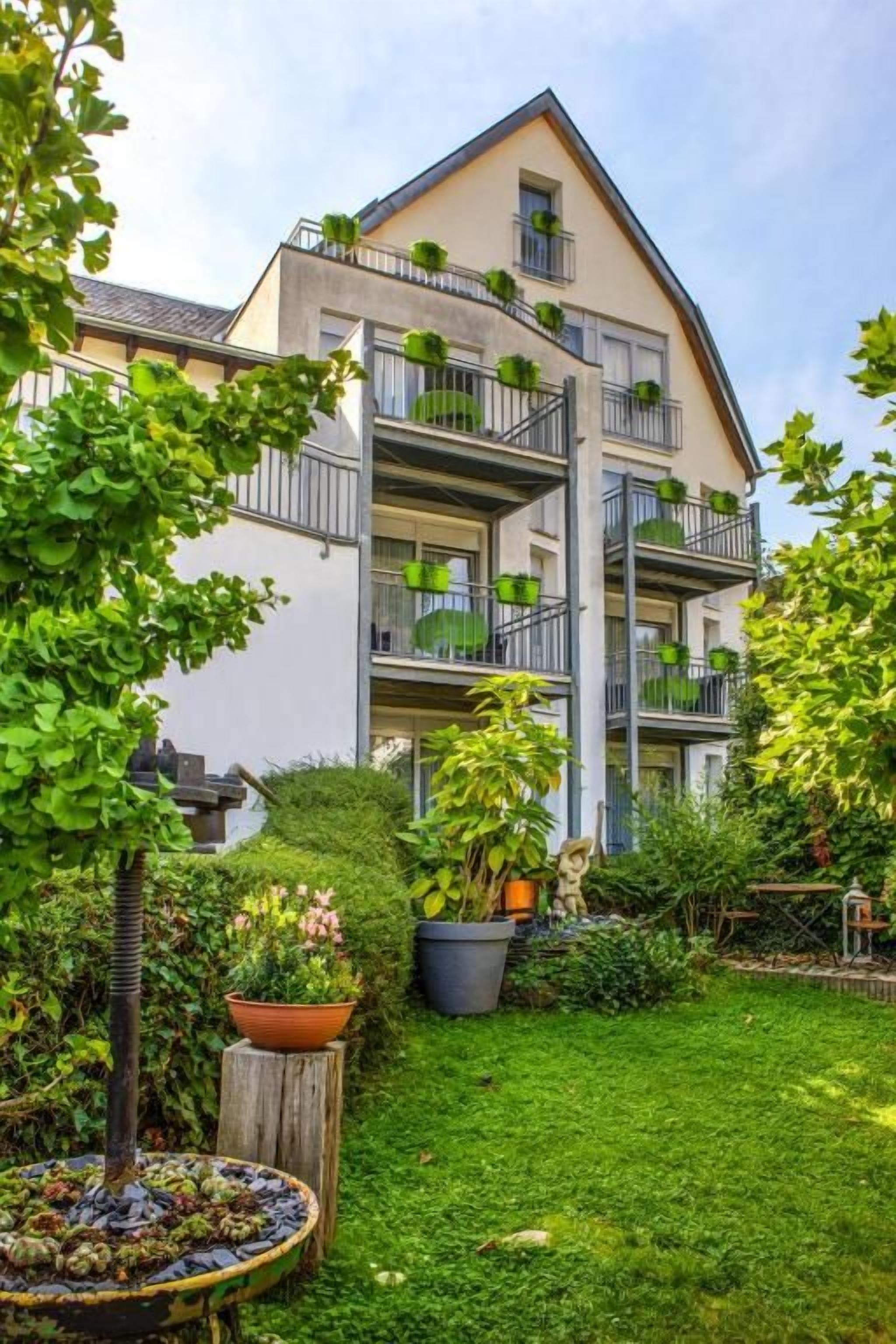 Ein mehrstöckiges Gebäude mit Balkonen, einem gepflegten Garten und blauem Himmel.