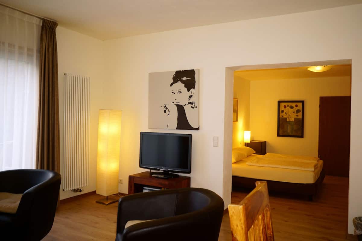 A hotel room with a flat-screen TV, a large floor lamp, a painting, a bed, and a wooden chair.
