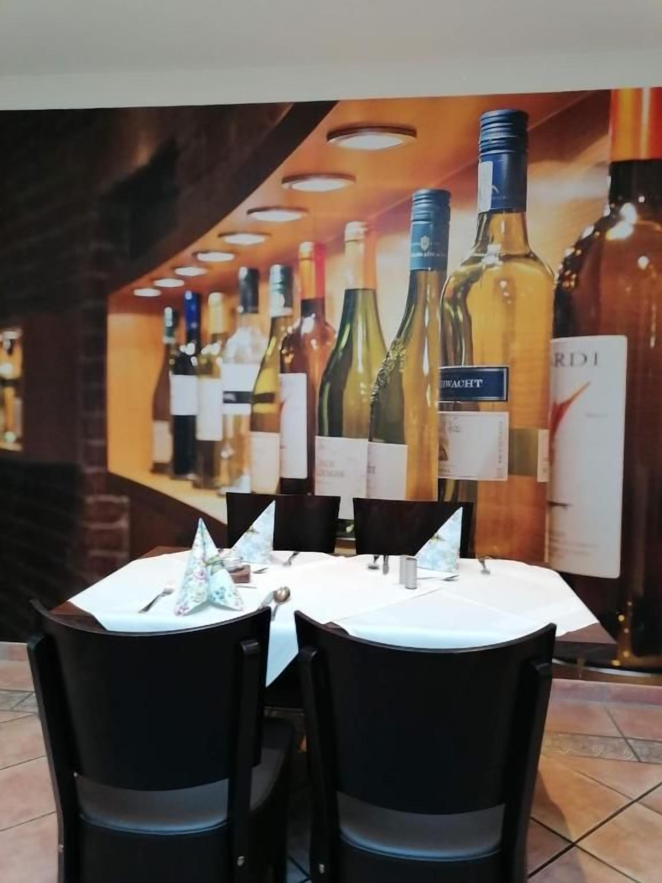 A restaurant interior with a white table, black chairs, and a backdrop of wine bottles.