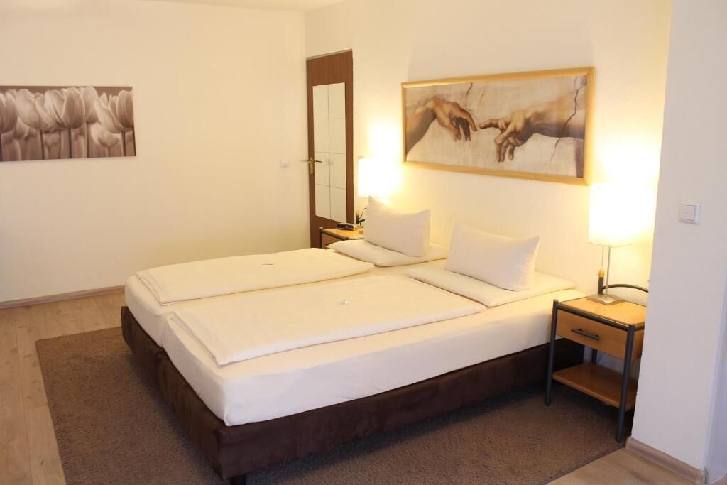 Een tweepersoonsbed met witte lakens, een nachtkastje met een lamp en een schilderij aan de muur.