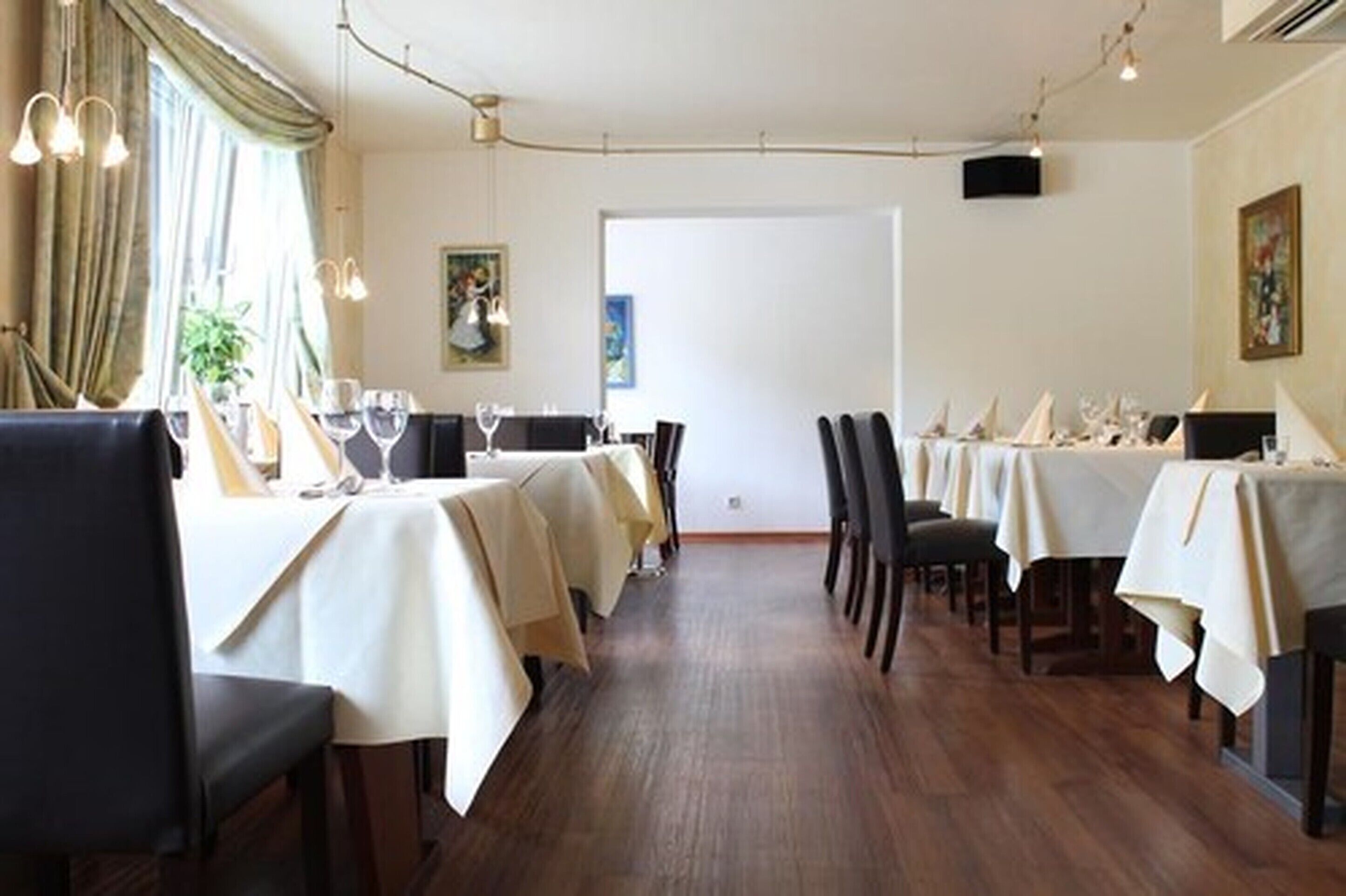 Une salle à manger avec des tables dressées pour le service, des chaises et un plancher en bois.