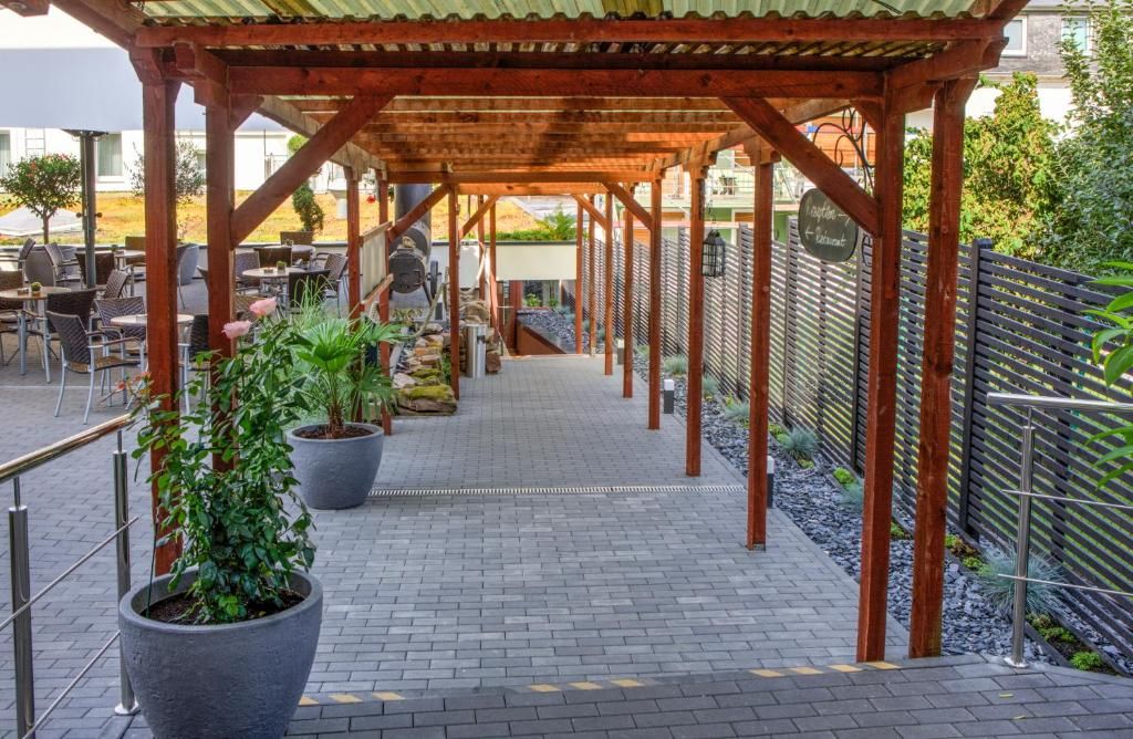 An outdoor patio area with a wooden pergola, seating arrangements, and potted plants.
