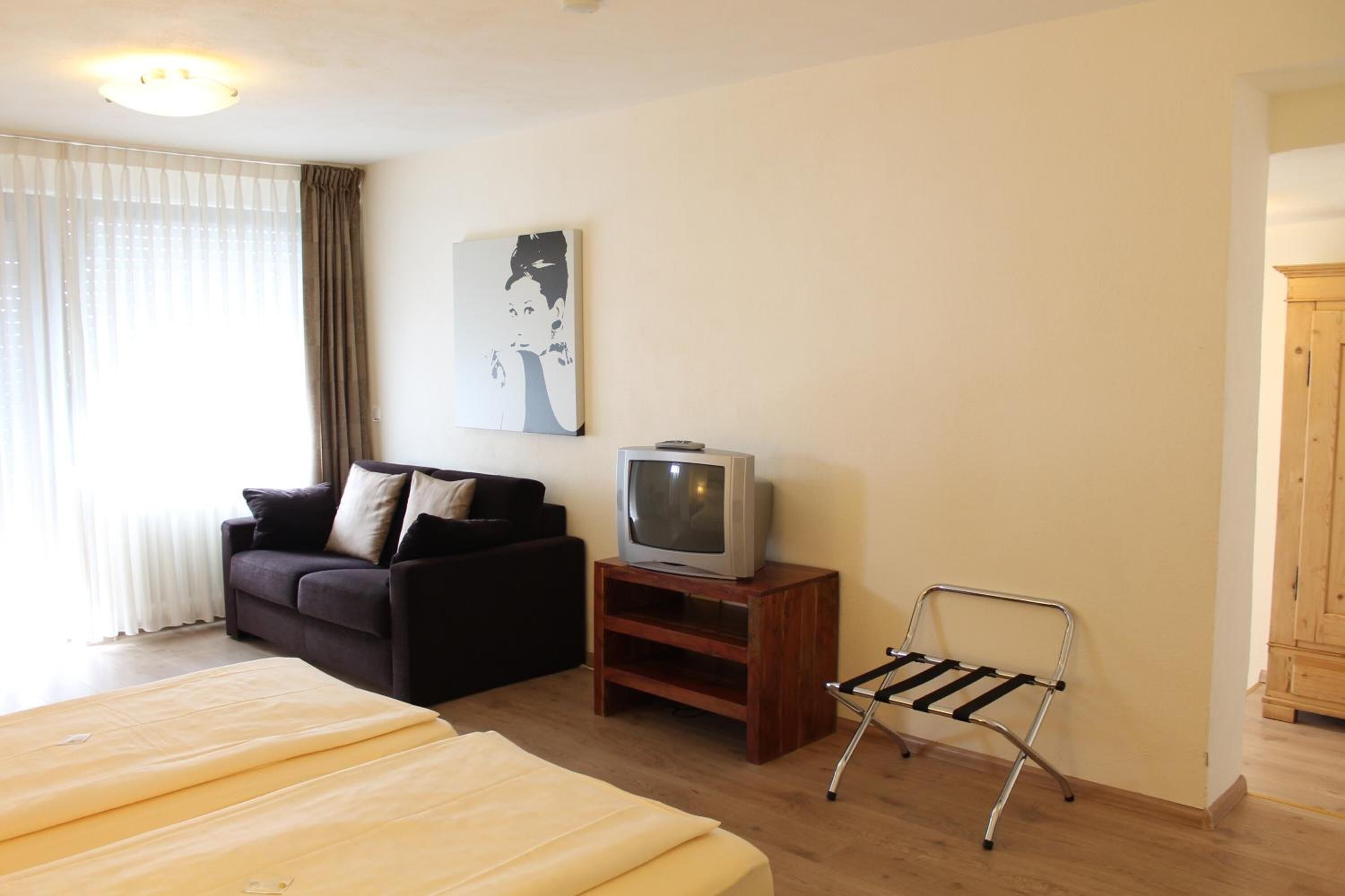 Een hotelkamer met een bed, een bank, een televisie op een houten standaard en een metalen stoel.