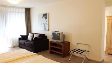 Een hotelkamer met een bed, een bank, een televisie op een houten standaard en een metalen stoel.
