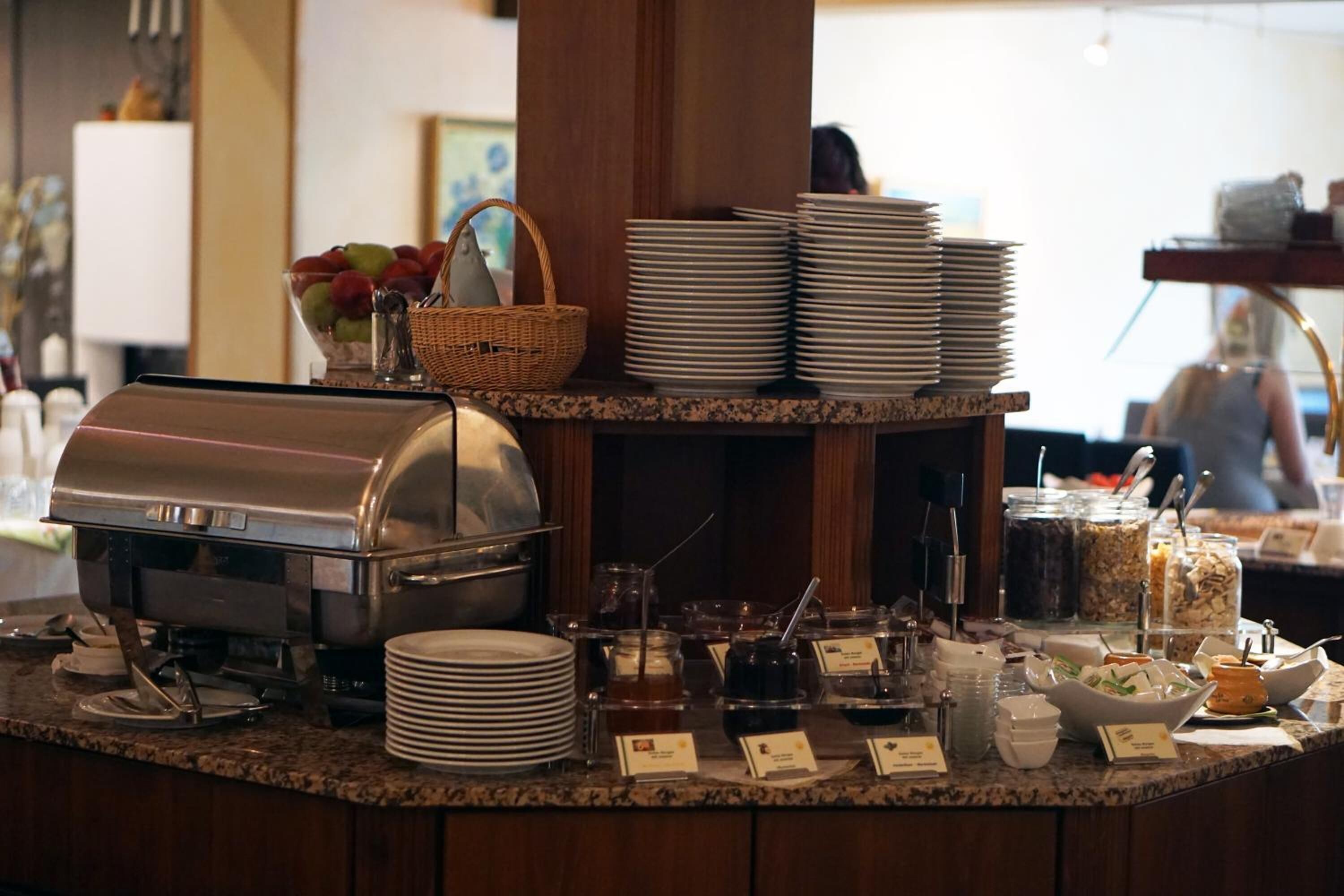 A buffet setup with a coffee station, stacked plates, and various food containers.