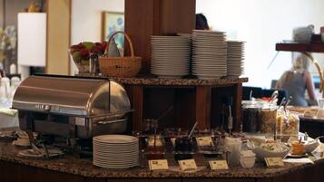 A buffet setup with a coffee station, stacked plates, and various food containers.