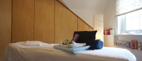 A bedroom with a bed, a wooden wardrobe, a window, and a bedside table with toiletries.