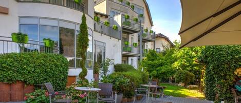 Un patio con mesas al aire libre, un edificio con balcones y una sombrilla grande.
