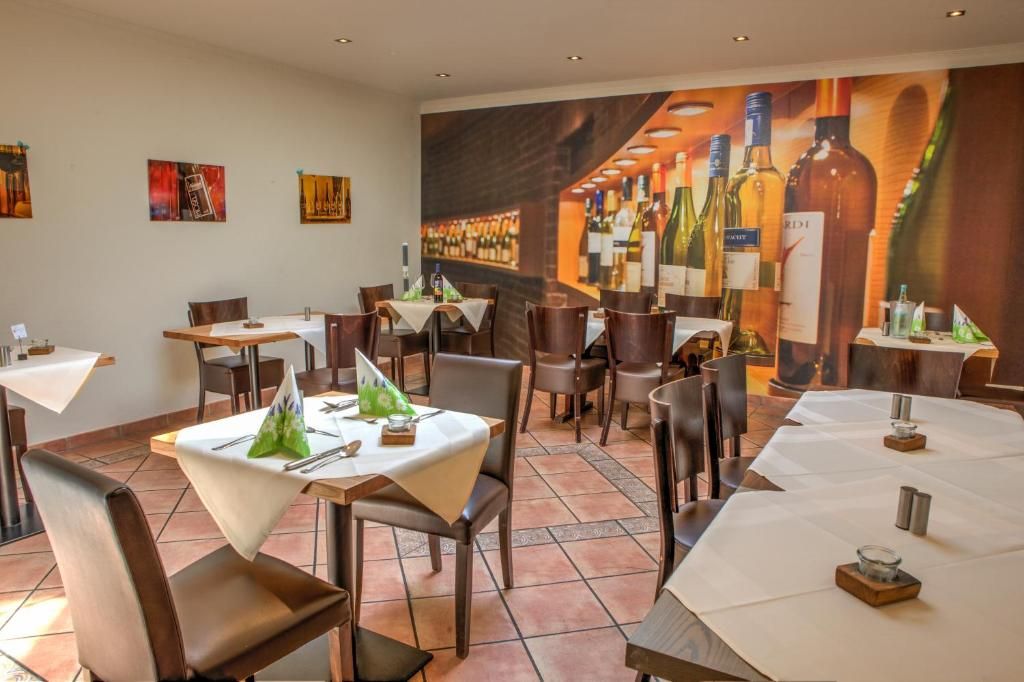 Een restaurantinterieur met meerdere tafels en stoelen, een muurschildering van wijnflessen en een betegelde vloer.