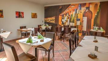 Een restaurantinterieur met meerdere tafels en stoelen, een muurschildering van wijnflessen en een betegelde vloer.