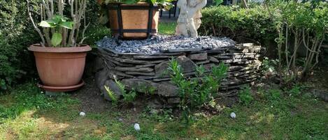 Un jardín con plantas en macetas, una escultura de piedra y un muro de piedra.