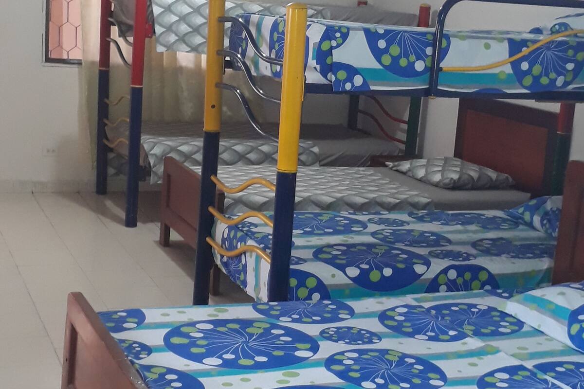 Une chambre de dortoir avec des lits superposés, une fenêtre ornée d’un motif hexagonal et un rideau.