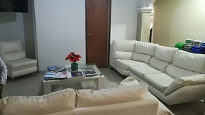 A living room with a sofa, a coffee table with magazines, a TV, and a door marked "BAÑO". - Hotel Granada Inn (Barranquilla)