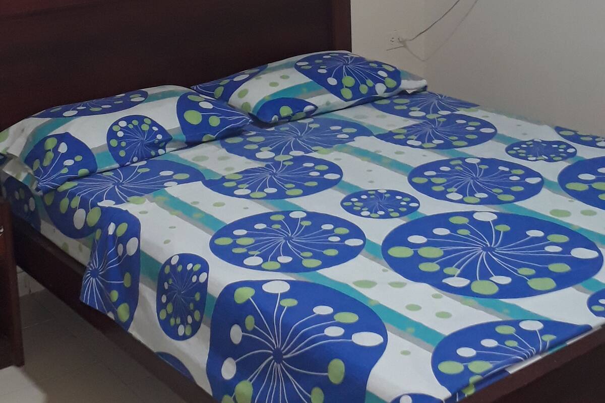 Une chambre à coucher avec un lit, un ventilateur fixé au mur et un tableau encadré.