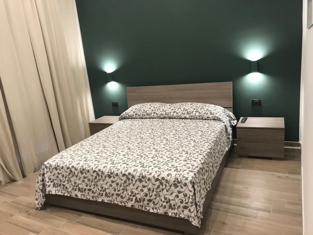 A neatly made bed with a patterned bedspread, two bedside tables with lamps, and a wooden floor.