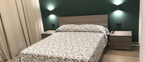 A neatly made bed with a patterned bedspread, two bedside tables with lamps, and a wooden floor.