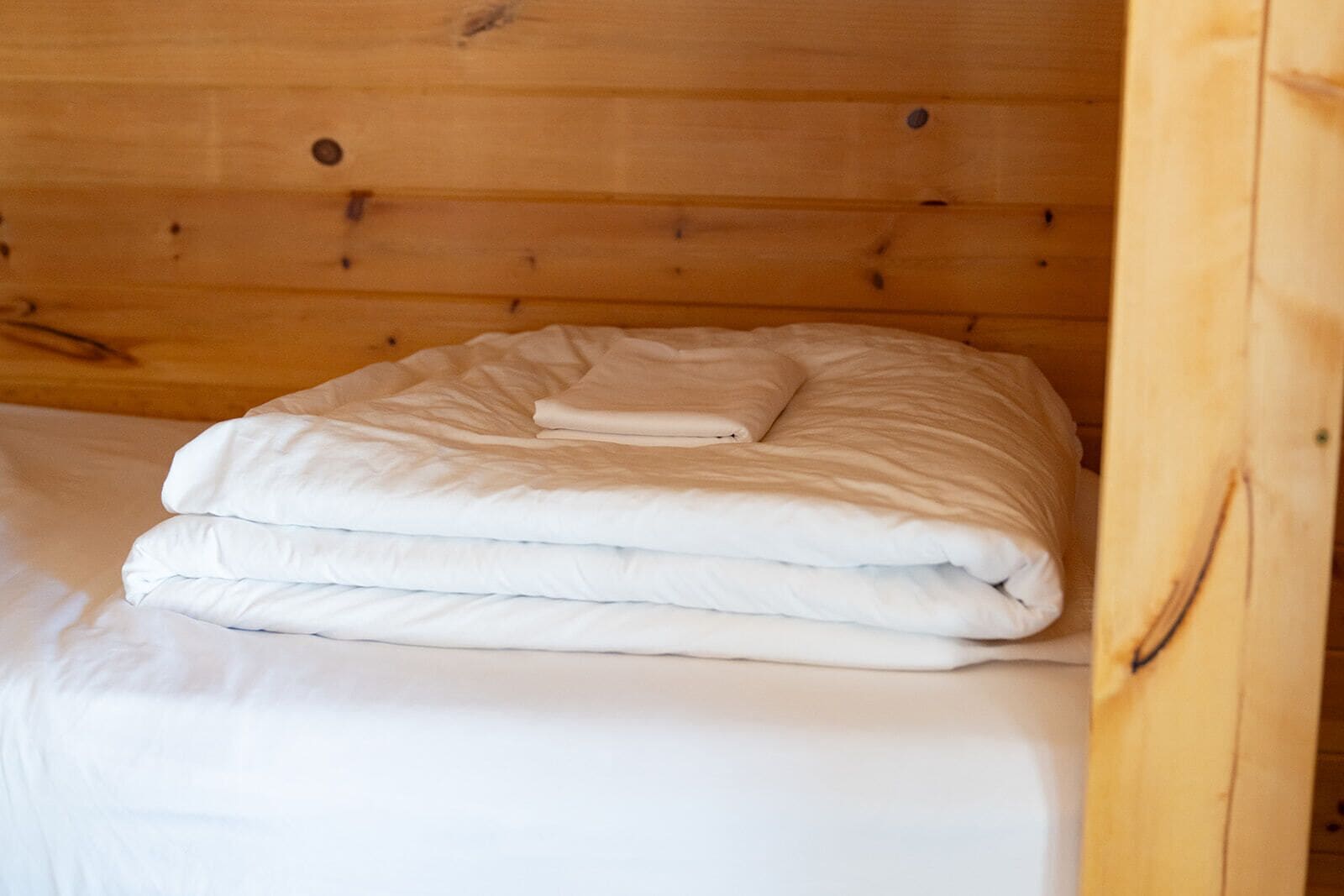 Una cama bien hecha con sábanas blancas en una habitación tipo cabaña de madera.