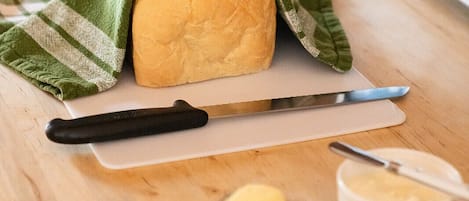 A loaf of bread on a cutting board with a knife, a butter dish, and a bowl of jam.