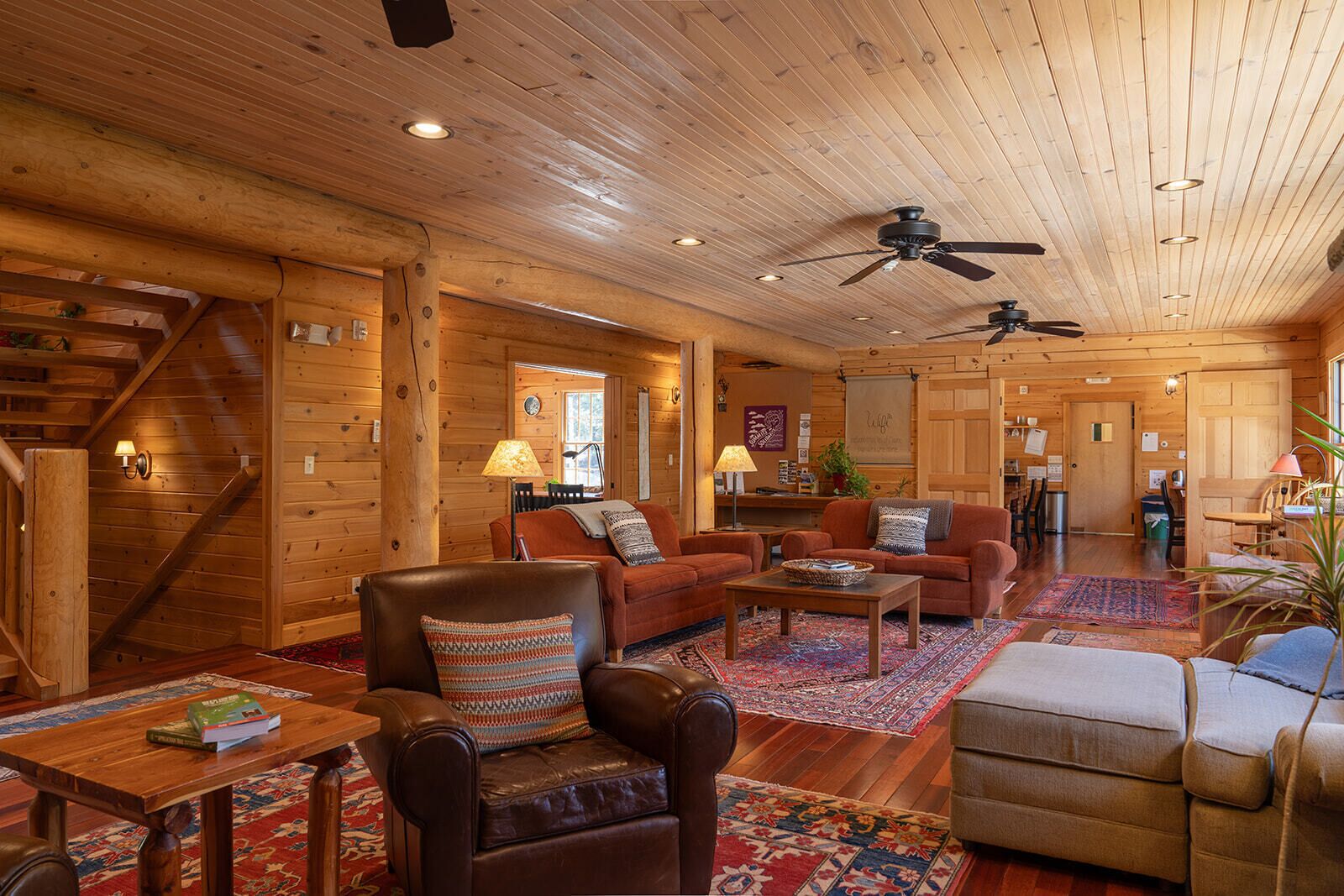 A spacious log cabin interior with a living room, dining area, and kitchen. There are multiple seating arrangements, including a sofa set, a dining table, and a kitchen counter.