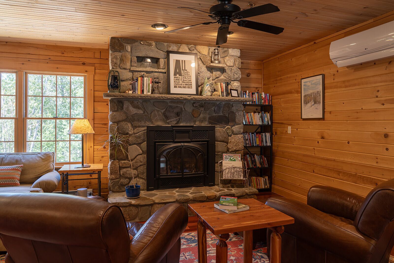 A cozy cabin interior with a stone fireplace, leather furniture, and a bookshelf.