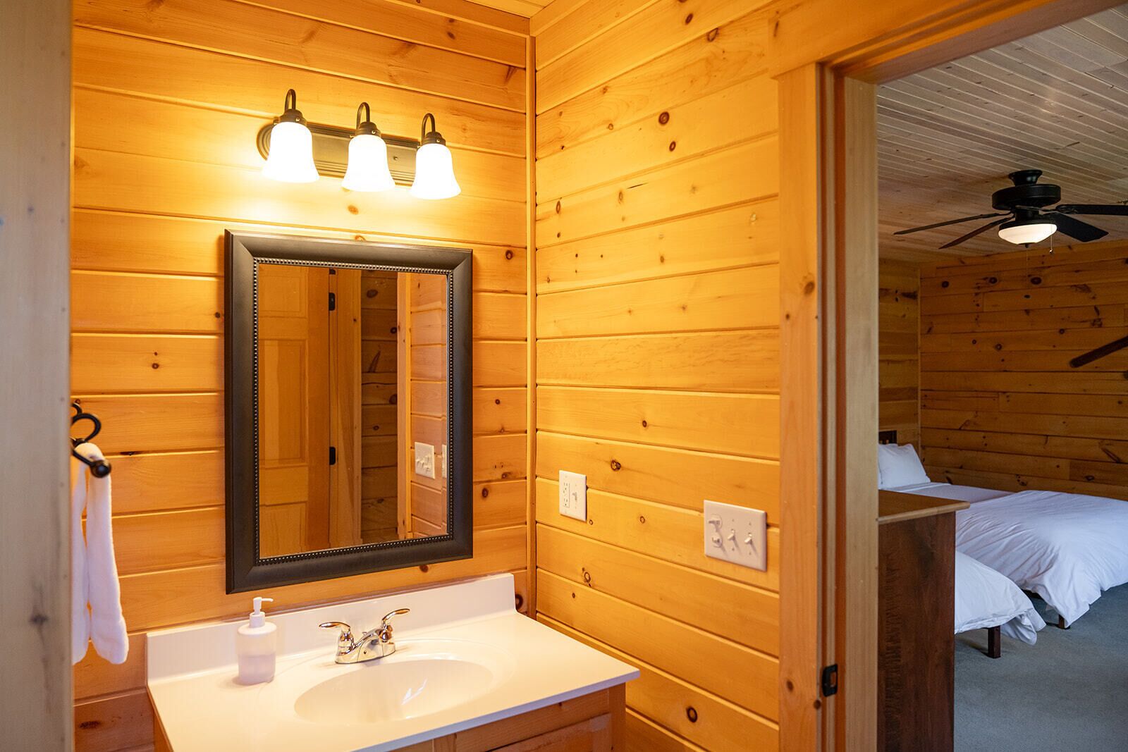 Un baño al estilo cabaña de madera con lavamanos, espejo y tres luces fijadas a la pared.