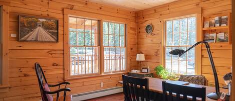 L’intérieur chaleureux d’un chalet avec des murs en bois, de grandes fenêtres, un fauteuil à bascule, un bureau avec une lampe et une bibliothèque.
