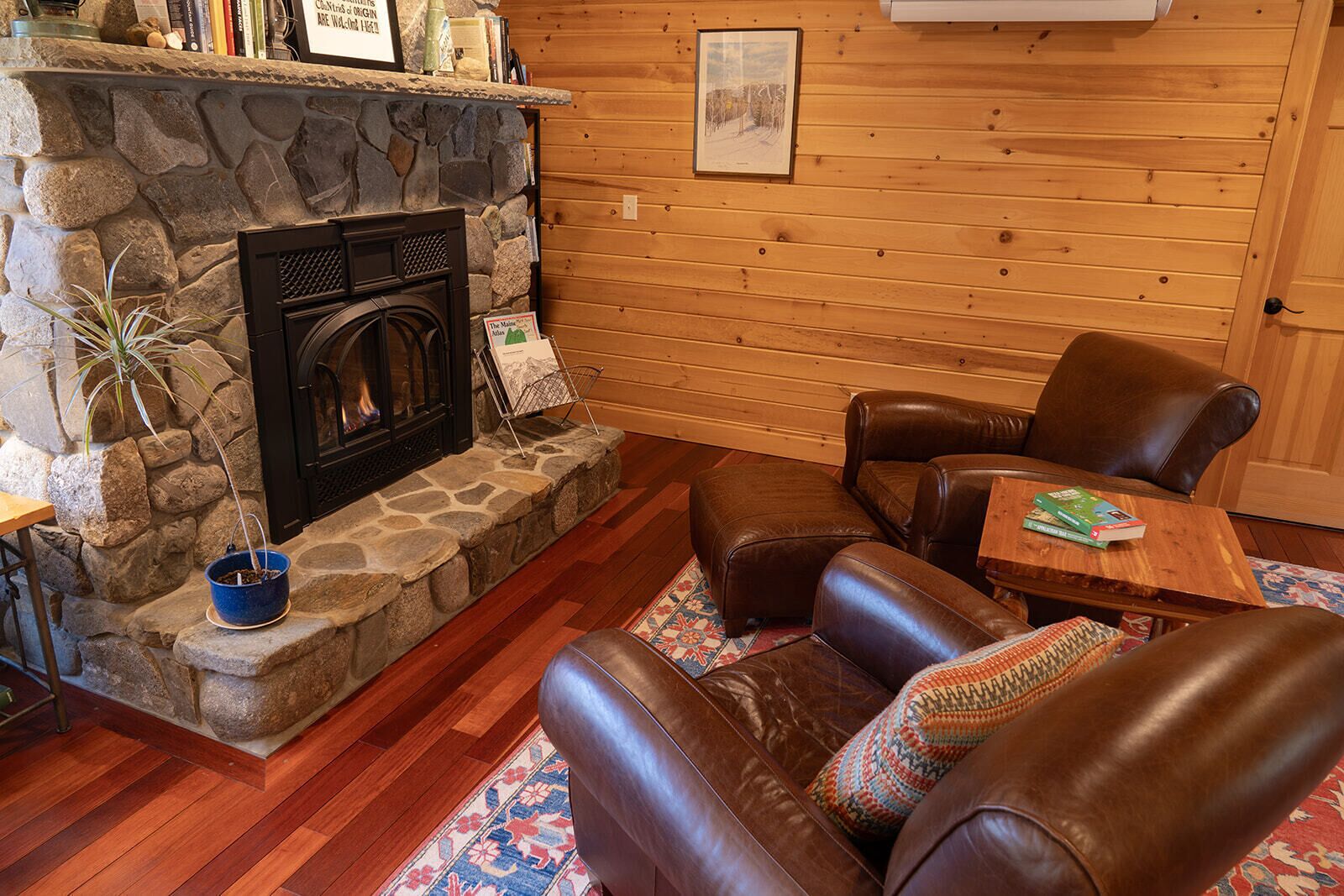 A cozy living room with a stone fireplace, leather sofas, and a wooden floor.