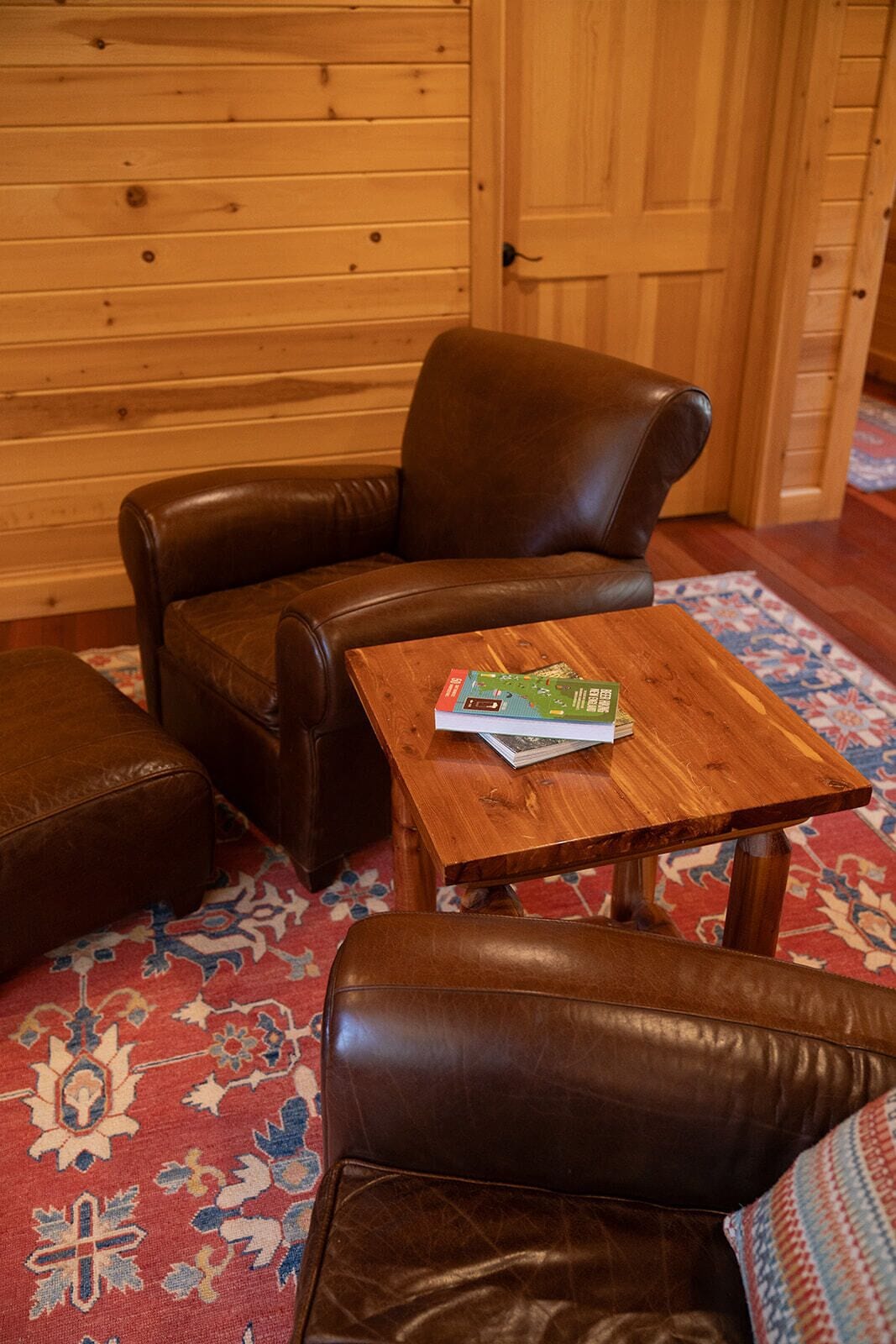Un interior de madera con un sillón de cuero marrón, un reposapiés a juego y una mesa de centro de madera con un libro.