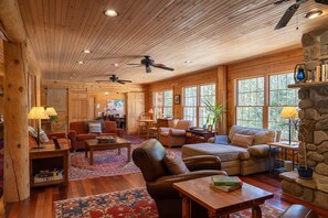 A cozy cabin interior with wooden walls, a stone fireplace, and a large window overlooking greenery. - Hostel Of Maine (Kingfield)