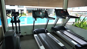 Een sportschool met loopbanden en een elliptische machine, met uitzicht op een zwembad.