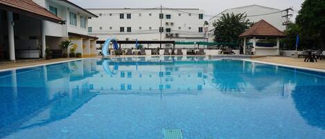 A swimming pool with tiled flooring, a water slide, and lounge chairs.