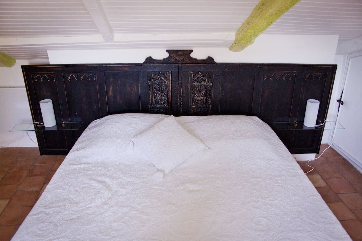Ein Schlafzimmer mit einem großen Bett, einem dunklen Holzkopfteil, zwei Nachttischen und einer weißen Wand.