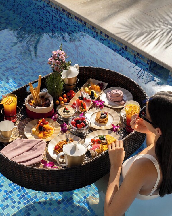 A dining setup by a pool with a variety of foods and drinks.