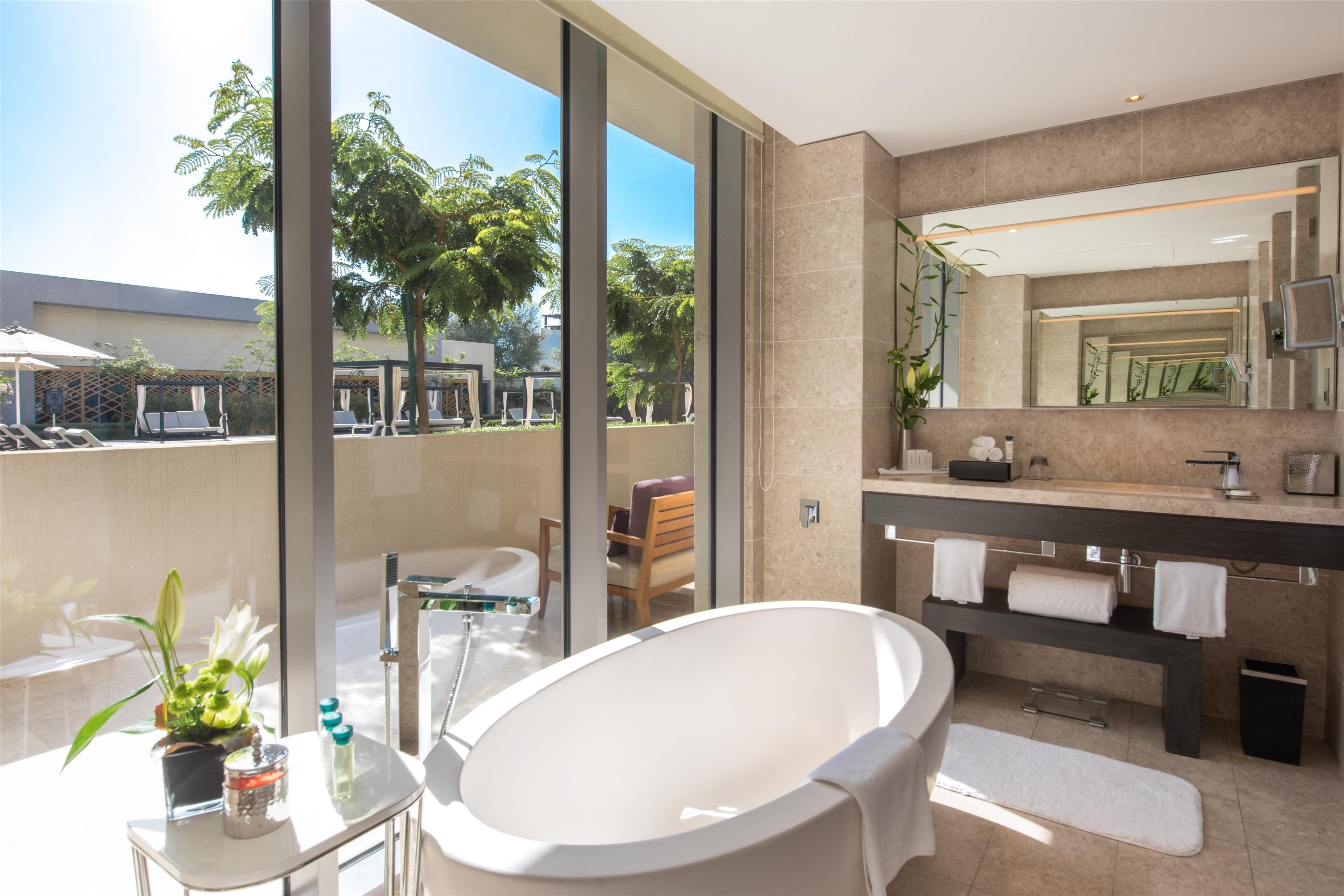 A modern bathroom with a freestanding bathtub, a large mirror, and a view of the outdoor area.